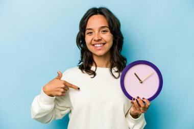 Mavi arka planda bir saat tutan genç İspanyol kadın gömleğin fotokopi odasını elle gösteriyor, gururlu ve kendinden emin.