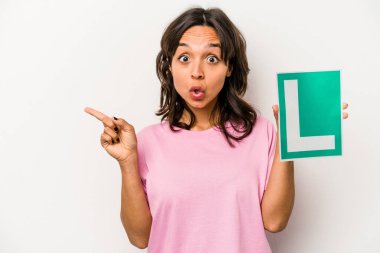 Beyaz arka planda, elinde acemi sürücü tabelası tutan Latin bir kadın var.