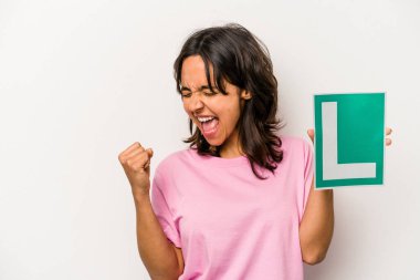 Genç İspanyol kadın elinde acemi sürücü işareti ile beyaz arka planda izole bir şekilde zafer kazandıktan sonra yumruğunu kaldırıyor, kazanan konsept.