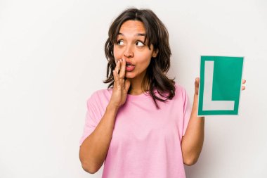 Beyaz arka planda izole edilmiş acemi sürücü tabelasını tutan genç İspanyol kadın gizli bir sıcak fren haberinden bahsediyor ve yana bakıyor.