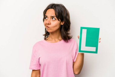 Beyaz arka planda izole edilmiş acemi sürücü tabelasını tutan genç İspanyol kadın şaşkın ve güvensiz hissediyor..