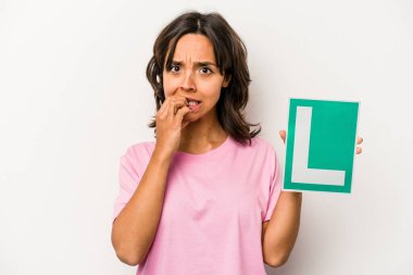 Beyaz arka planda izole edilmiş, tırnak yiyen, gergin ve endişeli, acemi sürücü tabelasını tutan genç İspanyol kadın..