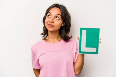 Genç İspanyol kadın elinde acemi sürücü işareti ile beyaz arka planda izole edilmiş hedeflere ve amaçlara ulaşma hayali kuruyor.