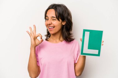 Genç İspanyol kadın elinde acemi sürücü işareti tutuyor. Beyaz arka planda izole edilmiş, neşeli ve kendinden emin..