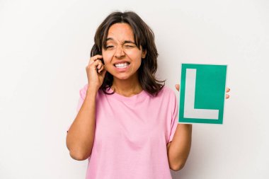 Genç İspanyol kadın elinde acemi sürücü tabelası var. Beyaz arka planda izole edilmiş, kulakları elleriyle kapatıyor..