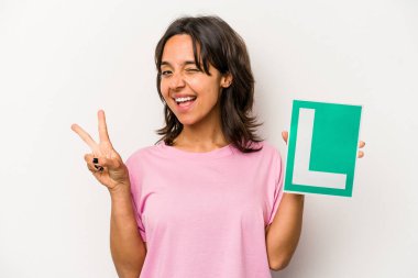 Genç İspanyol kadın elinde acemi sürücü işareti ile beyaz arka planda izole edilmiş neşeli ve kaygısız parmaklarıyla barış sembolü gösteren.