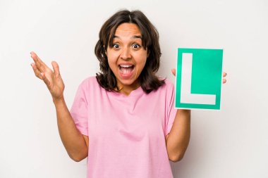 Genç İspanyol kadın, beyaz arka planda izole edilmiş acemi sürücü tabelasını tutuyor. Hoş bir sürprizle karşılaşıyor, heyecanlı ve el kaldırıyor..