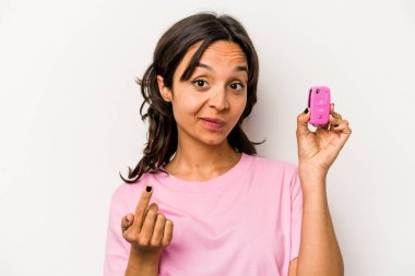 Beyaz arka planda izole edilmiş araba anahtarlarını tutan genç İspanyol kadın sanki seni davet ediyormuş gibi seni işaret ediyor..