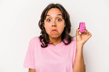 Beyaz arka planda izole edilmiş araba anahtarlarını tutan genç İspanyol kadın omuzlarını silker ve gözleri açık kalır..