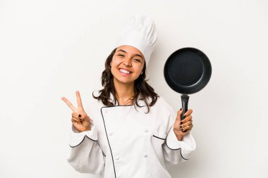 Genç İspanyol aşçı kadın beyaz arka planda izole edilmiş neşeli ve kaygısız parmaklarıyla barış sembolü gösteriyor..