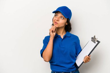 Beyaz arka planda izole edilmiş genç İspanyol kadın teslimatçı şüpheli ve şüpheci bir ifadeyle yana bakıyor..