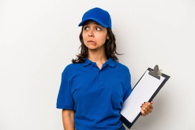 Beyaz arka planda izole edilmiş genç İspanyol kadın teslimatçı kafası karışmış, şüpheli ve güvensiz hissediyor..