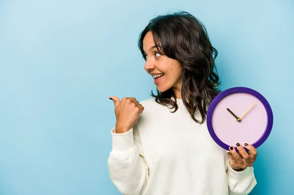 Young Hispanic Woman Holding Clock Isolated Blue Background Points Thumb — Foto de Stock