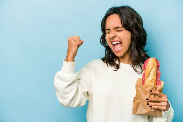 Ung Latinamerikansk Kvinna Äter Smörgås Isolat Blå Bakgrund Höja Näve — Stockfoto