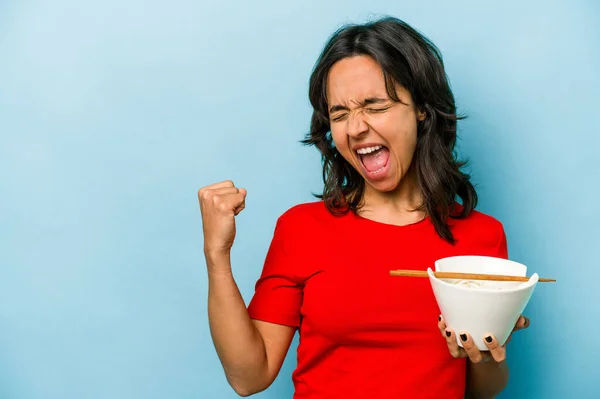 Young Hispanic Woman Eating Noodles Isolated Blue Background Raising Fist — Stockfoto