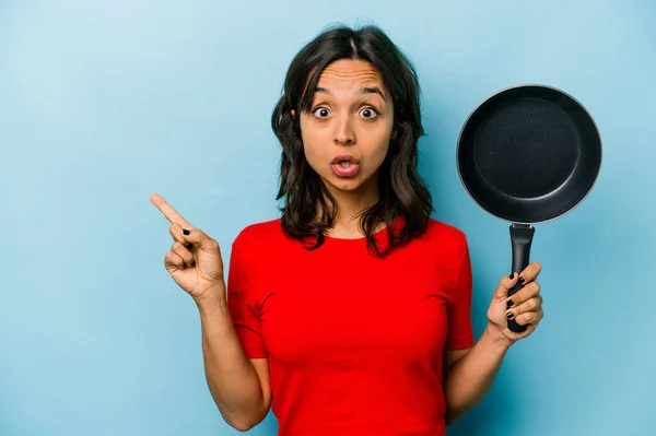 Ung Latinamerikansk Kvinna Håller Stekpanna Isolerad Blå Bakgrund Pekar Sidan — Stockfoto