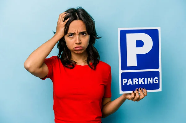 Young hispanic woman holding parking placard isolated on blue background being shocked, she has remembered important meeting.