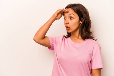 Beyaz arka planda izole edilmiş genç İspanyol kadın uzaklara bakıyor ve elini alnına koyuyor..