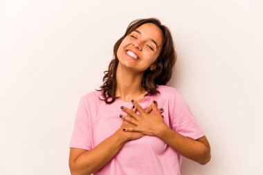 Beyaz arka planda izole edilmiş genç İspanyol kadın gülüyor, ellerini kalbe koyuyor, mutluluk kavramını koruyor..