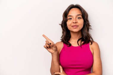Beyaz arka planda izole edilmiş genç İspanyol kadın işaret parmağıyla işaret ederek gülümsüyor..