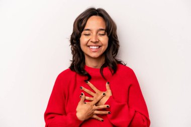 Beyaz arka planda izole edilmiş genç İspanyol kadın mutlu bir şekilde gülüyor ve ellerini karnının üstünde tutarak eğleniyor..