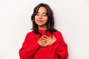 Beyaz arka planda izole edilmiş genç İspanyol kadın gülüyor, ellerini kalbe koyuyor, mutluluk kavramını koruyor..