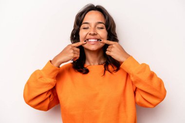 Beyaz arka planda izole edilmiş genç İspanyol kadın gülümsüyor, parmaklarını ağıza doğrultuyor..