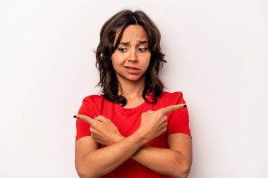 Beyaz arka planda izole edilmiş genç İspanyol kadın iki seçenek arasında seçim yapmaya çalışıyor..