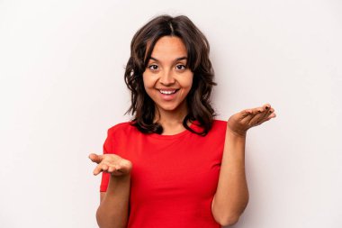 Beyaz arka planda izole edilmiş genç İspanyol kadın kollarıyla ölçeği yapıyor, mutlu ve kendinden emin hissediyor..