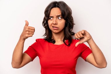 Latin kökenli genç bir kadın beyaz arka planda izole edilmiş, baş parmağını kaldırıyor, zor seçim konsepti.