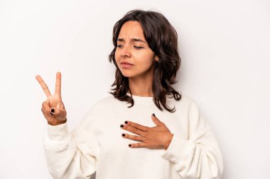 Beyaz arka planda izole edilmiş genç İspanyol kadın yemin ediyor, elini göğsüne koyuyor..