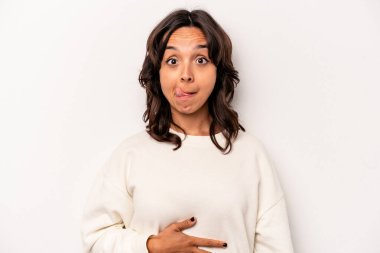 Beyaz arka planda izole edilmiş genç İspanyol kadın karnına dokunuyor, nazikçe gülümsüyor, yemek yiyor ve tatmin oluyor..