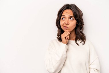 Beyaz arka planda izole edilmiş genç İspanyol kadın şüpheli ve şüpheci bir ifadeyle yana bakıyor..