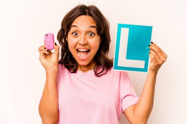 Latin kökenli genç bir kadın elinde başlangıç levhası ve mavi arka planda izole edilmiş anahtar bir araba tutuyor.