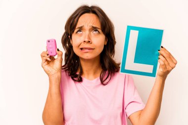 Latin kökenli genç bir kadın elinde başlangıç levhası ve mavi arka planda izole edilmiş anahtar bir araba tutuyor.