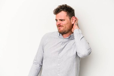 Beyaz arka planda izole edilmiş genç beyaz bir adam yorgun ve uykulu bir şekilde elini başının üstünde tutuyor..