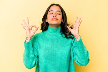 Sarı arka planda izole edilmiş genç İspanyol kadın sıkı çalışma gününden sonra rahatlıyor, yoga yapıyor..