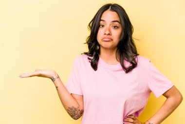 Sarı arka planda izole edilmiş genç İspanyol kadın bir avuç içinde fotokopi alanı ve belinde bir el daha gösteriyor..
