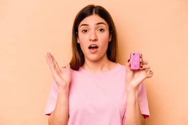 Latin kökenli genç bir kadın elinde bej arka planda izole edilmiş bir araba tutuyor. Şaşırmış ve şok olmuş..