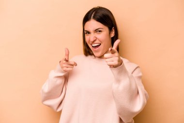 Genç İspanyol kadın, bej arka planda izole edilmiş, gülümseyen, ön tarafı işaret eden..