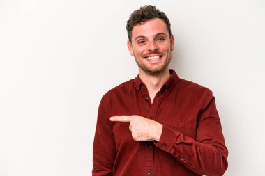 Beyaz arka planda izole edilmiş genç beyaz bir adam gülümsüyor ve boş alanda bir şeyler gösteriyor..
