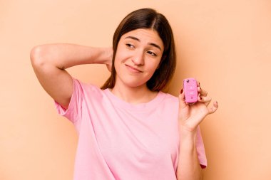 Latin kökenli genç bir kadın bej arka planda izole edilmiş bir araba tutuyor. Kafasının arkasına dokunuyor, düşünüyor ve bir seçim yapıyor..