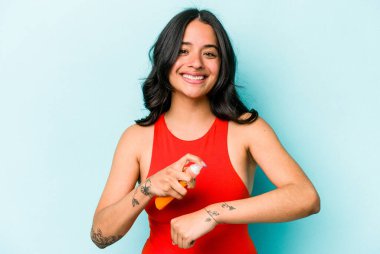 Mavi arka planda güneş kremi tutan genç İspanyol kadın.