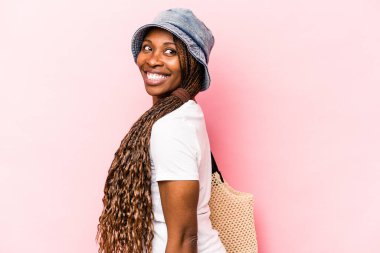 Genç Afrikalı Amerikalı bir kadın pembe arka planda izole bir şekilde sahile gidiyor. Gülümsüyor, neşeli ve keyifli görünüyor..