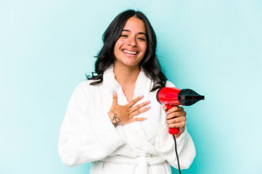 Mavi arka planda izole edilmiş kurutma makinesini tutan genç İspanyol kadın kahkahalarla gülüyor..