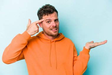 Kafkasyalı genç adam mavi arka planda izole edilmiş ve elinde bir ürün tutuyor..