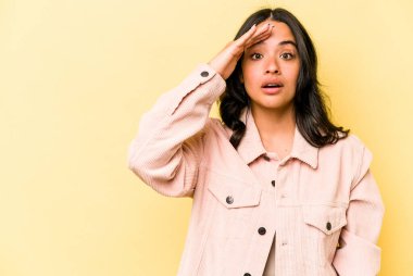 Sarı arka planda izole edilmiş genç İspanyol kadın yüksek sesle bağırıyor, gözleri açık ve elleri gergin tutuyor..