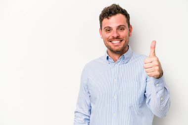Beyaz arka planda izole edilmiş genç beyaz adam gülümsüyor ve başparmağını kaldırıyor.