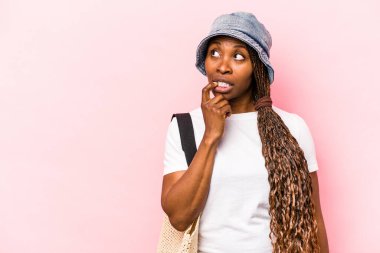 Genç Afrikalı Amerikalı bir kadın plaja gidiyor. Pembe arka planda izole edilmiş. Bir şeyin fotokopi odasına baktığını düşünüyor..