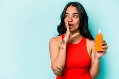 Mavi arka planda güneş kremi tutan genç İspanyol kadın gizli bir sıcak fren haberi veriyor ve yan bakıyor.